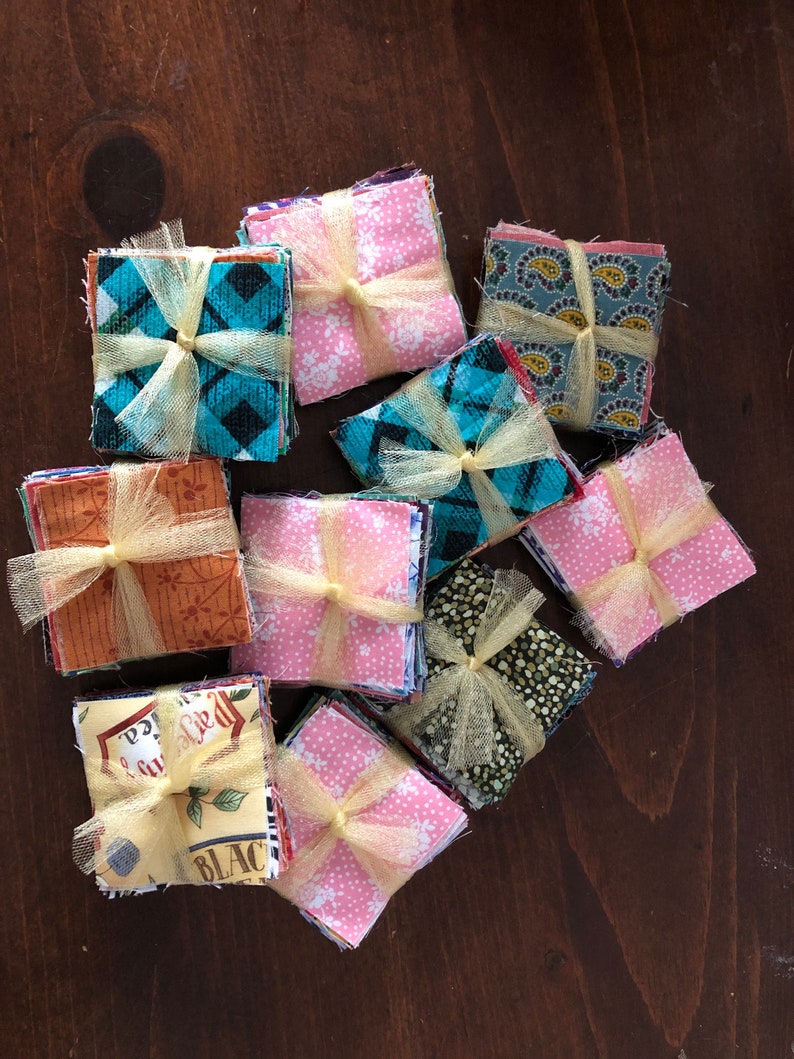 May include: A collection of fabric squares, each tied with a yellow ribbon, are stacked on a wooden surface. The fabric squares are in various patterns and colors, including pink, blue, green, and brown.