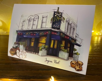 Może przedstawiać: Kartka świąteczna z ręcznie rysowaną ilustracją kawiarni z niebieskim daszkiem i napisem "Le Delice" nad wejściem. Kawiarnia jest ozdobiona świątecznymi lampkami, a przed nią stoją bałwany. Na kartce znajduje się również napis "Joyeux Noel" i kilka pierogów z mięsem.