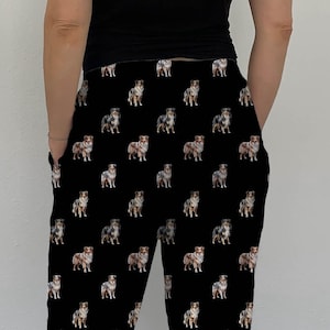 May include: Black sweatpants with a repeating pattern of Australian Shepherd dogs. The dogs are all facing forward and have a variety of colors and markings.