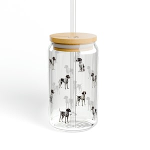 May include: A clear glass tumbler with a bamboo lid and a clear straw. The tumbler is decorated with a repeating pattern of black and white dog illustrations. The tumbler is designed for cold beverages.