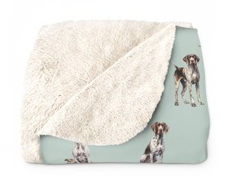 May include: A soft, plush throw blanket with a light blue background and a repeating pattern of brown and white German Shorthaired Pointers. The blanket has a white sherpa fleece on the reverse side.