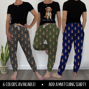 May include: Three pairs of sweatpants in gray, olive green, and navy blue, each patterned with a repeating image of a dog. The models are wearing black t-shirts. The text at the bottom says "6 COLORS AVAILABLE!" and "ADD A MATCHING SHIRT!"