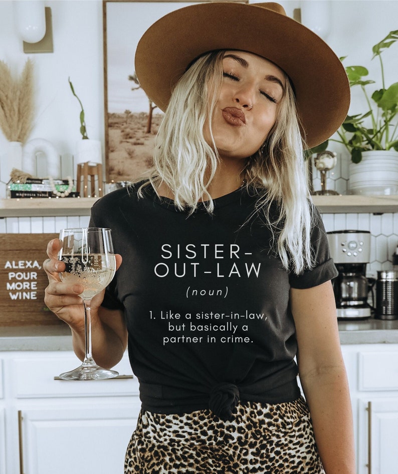 May include: A black t-shirt with white text that reads "Sister-Out-Law (noun) 1. Like a sister-in-law, but basically a partner in crime."