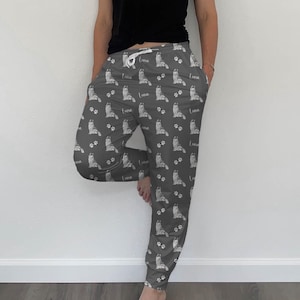 Op de afbeelding: Grijze sweatpants met een wit, herhalend patroon van een hond en de naam "Luna" erop gedrukt.