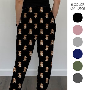 May include: Black pajama pants featuring a repeating pattern of brown and white puppies. The pants have pockets and the text "6 COLOR OPTIONS!" is visible. The available colors are black, pink, gray, navy, olive, and charcoal.