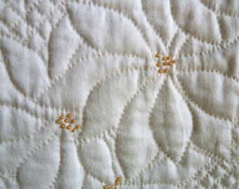 May include: Close-up of a white quilted fabric with a pattern of small, evenly spaced, golden stitches forming a flower design.