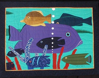 May include: A colorful quilted wall hanging featuring a variety of fish in a turquoise blue ocean scene. The fish are purple, brown, green, and black. The scene includes red coral and white bubbles.