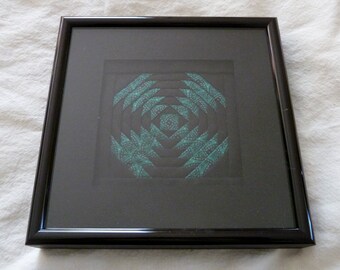 May include: A framed black and teal quilt square with a geometric pattern. The quilt square is framed in a black frame with a glossy finish.