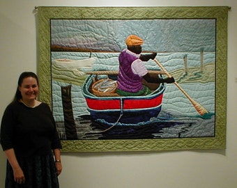 May include: A quilted wall hanging depicting a person in a boat rowing on a body of water. The person is wearing a purple vest and a brown hat. The boat is blue and red with a basket of fish in the front. The background is a light blue sky with a few clouds.
