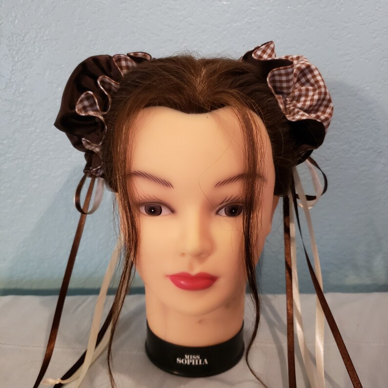 May include: Brown and white gingham hair scrunchies with brown satin ribbon ties. The scrunchies are worn on a mannequin head with brown hair.