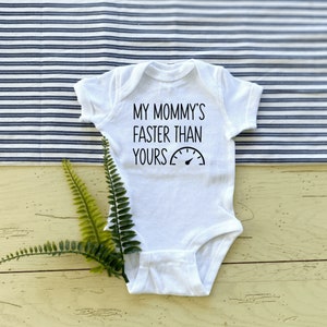 Könnte beinhalten: Weißer Baby-Strampler mit schwarzem Text, der "Meine Mama ist schneller als deine" lautet, mit einem Tachometer-Grafik.