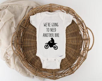 May include: White baby onesie with black text that reads "We're going to need another bike" and a silhouette of a person riding a dirt bike.