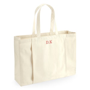 K&ouml;nnte beinhalten: Eine gro&szlig;e, cremefarbene Canvas-Tragetasche mit zwei Henkeln. Die Tasche hat ein rotes gesticktes Monogramm mit der Aufschrift "D.K."