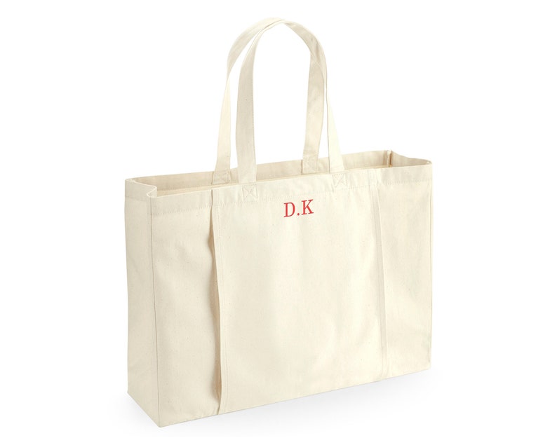 K&ouml;nnte beinhalten: Eine gro&szlig;e, cremefarbene Canvas-Tragetasche mit zwei Henkeln. Die Tasche hat ein rotes gesticktes Monogramm mit der Aufschrift "D.K."