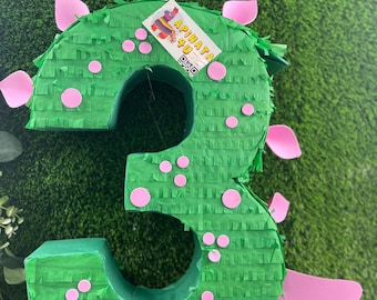 Könnte beinhalten: Eine grüne Piñata mit der Zahl drei und rosa Akzenten. Die Piñata ist mit rosa Kreisen und rosa Stacheln verziert. Die Piñata hat ein Etikett mit der Aufschrift "A Pinata 4 U".