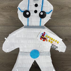 May include: White pinata shaped like a robot with blue and silver accents. The pinata has a silver glitter crown, blue stripes, and a blue circle on its chest. The pinata is labeled "Pinata 4 U" with a QR code.