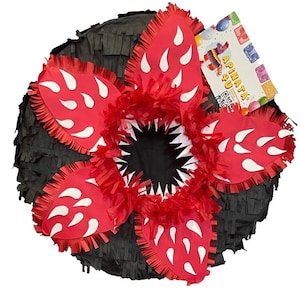 May include: A Demogorgon-themed piñata, featuring a black, fringed base with red, petal-like shapes. Each petal has white, teardrop-shaped accents. The center reveals a black mouth with white, jagged teeth. A tag with the text "APINATA 4U" is attached.