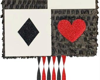 May include: A playing card-themed piñata with four card suits: clubs, spades, diamonds, and hearts. Each suit is a different color and texture. The piñata has black fringe around the edges and red and black streamers hanging from the bottom.