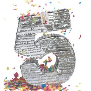May include: A silver number five piñata with colorful confetti. The piñata is made of a textured, metallic material. A small tag with text is attached to the top. Confetti in various colors is scattered around the base.