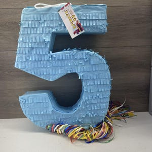 May include: A light blue number 5 shaped pinata with a colorful streamer tail. The pinata has a tag that says "Pinata #5".