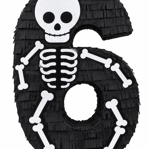May include: A number six shaped piñata covered in black fringe paper. The front features a white skull with black eye sockets and a nose, along with a white rib cage and white bone-shaped arms and legs attached to the black number structure.