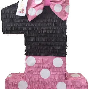 May include: A black and pink number one pinata with white polka dots. The pinata has a large pink bow with white polka dots on top.