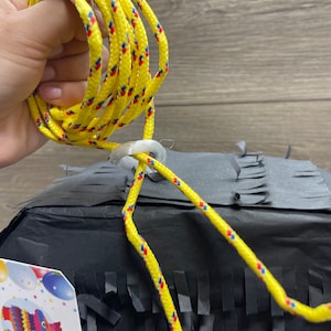 May include: A black pinata with yellow, red, and blue string attached to it. The pinata is decorated with black fringed paper.