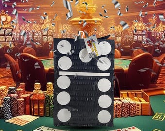 May include: Black and white domino-shaped pinata with white circles on a black background. The pinata is sitting on a green felt casino table with playing cards and chips.
