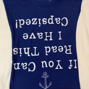 May include: A navy blue t-shirt with a white anchor and the text "If you can read this, I have a capsize!" printed on it.