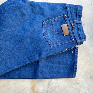 May include: A pair of blue denim jeans with a brown leather patch that says "Wrangler" on the back pocket.