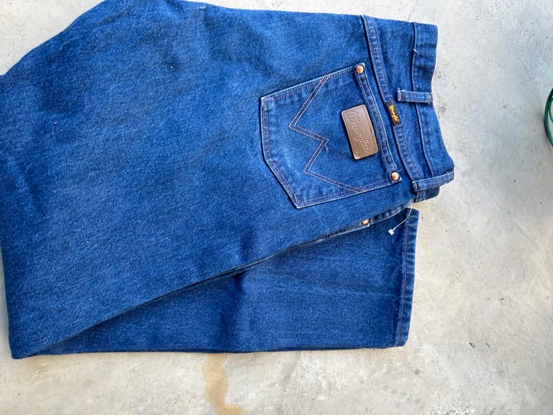 May include: A pair of blue denim jeans with a brown leather patch that says "Wrangler" on the back pocket.