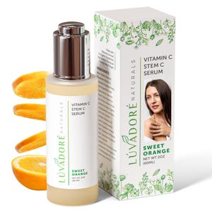 Puede incluir: Una botella de vidrio transparente con una tapa de bomba plateada llena de un líquido amarillo. La botella está etiquetada con "LÚVADORÉ NATURALS" y "VITAMIN C STEM C SERUM" con un aroma a naranja dulce. La botella está sobre un fondo blanco con rodajas de naranja alrededor. La botella está junto a una caja blanca con la misma etiqueta y la cara de una mujer.