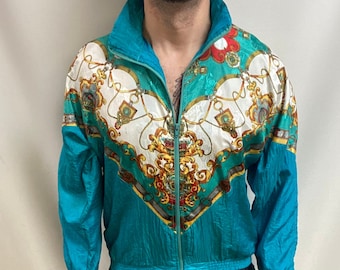 May include: A teal blue tracksuit with a white and gold patterned jacket. The jacket has a zipper closure and a stand-up collar.