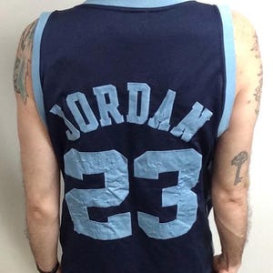 May include: Navy blue basketball jersey with light blue accents. The jersey features the name "JORDAN" and the number "23" in light blue lettering on the back. The jersey has a sleeveless design.