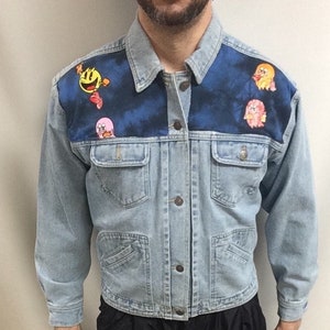 Könnte beinhalten: Eine hellblaue Jeansjacke mit einem Batik-Muster auf dem Rücken und bunten Comicfiguren-Patches auf den Schultern.