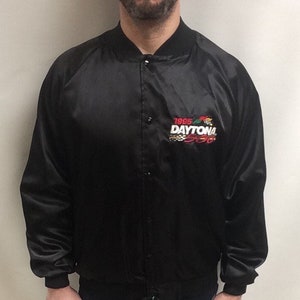 Może przedstawiać: Czarna satynowa kurtka bomberowa z haftowanym logo w kolorze białym i czerwonym, na którym widnieje napis "1995 DAYTONA 500".