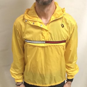 May include: A yellow hooded jacket with a red, white, and blue stripe across the chest. The jacket has a snap closure and a drawstring hood.