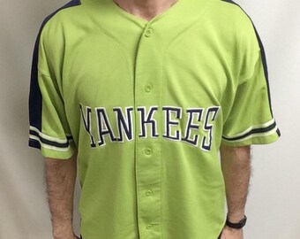 May include: A lime green baseball jersey with the word "YANKEES" across the chest in navy blue lettering. The jersey has navy blue accents on the shoulders and sleeves. The jersey is buttoned up and has short sleeves.
