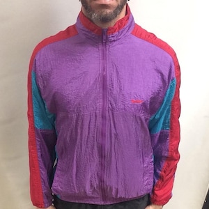 Könnte beinhalten: Eine Windbreaker-Jacke in Lila, Rot und Blau mit Reißverschluss. Die Jacke hat ein kleines Logo auf der Brust.