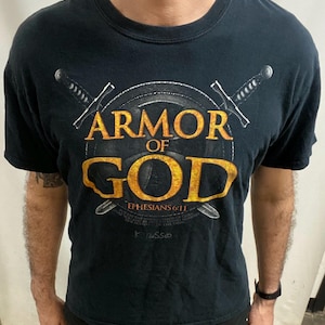 May include: Black t-shirt with the words "ARMOR OF GOD" in gold lettering, with a shield and two crossed swords design. The text "Ephesians 6:11" is below the shield.