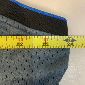 Puede incluir: Primer plano de una tela de malla gris con ribete negro y azul. Una cinta m&eacute;trica amarilla muestra una longitud de aproximadamente 56 a 61 cm. La tela tiene peque&ntilde;os agujeros espaciados.