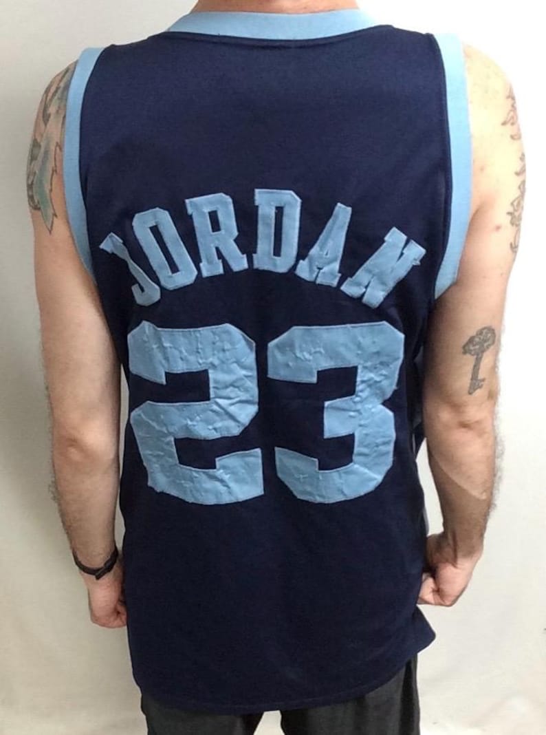 May include: Navy blue basketball jersey with light blue accents. The jersey features the name "JORDAN" and the number "23" in light blue lettering on the back. The jersey has a sleeveless design.