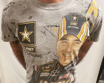 May include: Grey t-shirt with a large graphic of a smiling man in a U.S. Army hat and uniform. The shirt also displays the U.S. Army logo with the text "ARMY STRONG". The t-shirt has a crew neck and short sleeves.