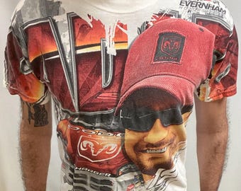 May include: White t-shirt with a graphic design featuring a red cap, sunglasses, and a smiling face. The shirt also displays the Dodge logo and the words "Evernham Motorsports".