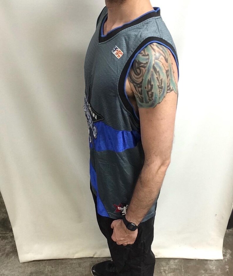 Puede incluir: Camiseta de baloncesto gris y azul con ribete negro. La camiseta presenta la palabra "Arizona" y un logotipo. La camiseta es sin mangas y tiene un dise&ntilde;o de cuello en V. La camiseta la lleva una persona.