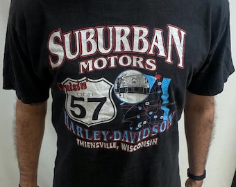 May include: Black Harley-Davidson t-shirt with a graphic featuring "Suburban Motors" and "Cruisin' 57". The design includes a road sign and a map, with text indicating Thiensville, Wisconsin.