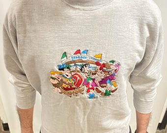May include: A light grey sweatshirt with a colourful embroidered design featuring characters and the text "Bedrock Stables". The design includes flags and cartoon figures.