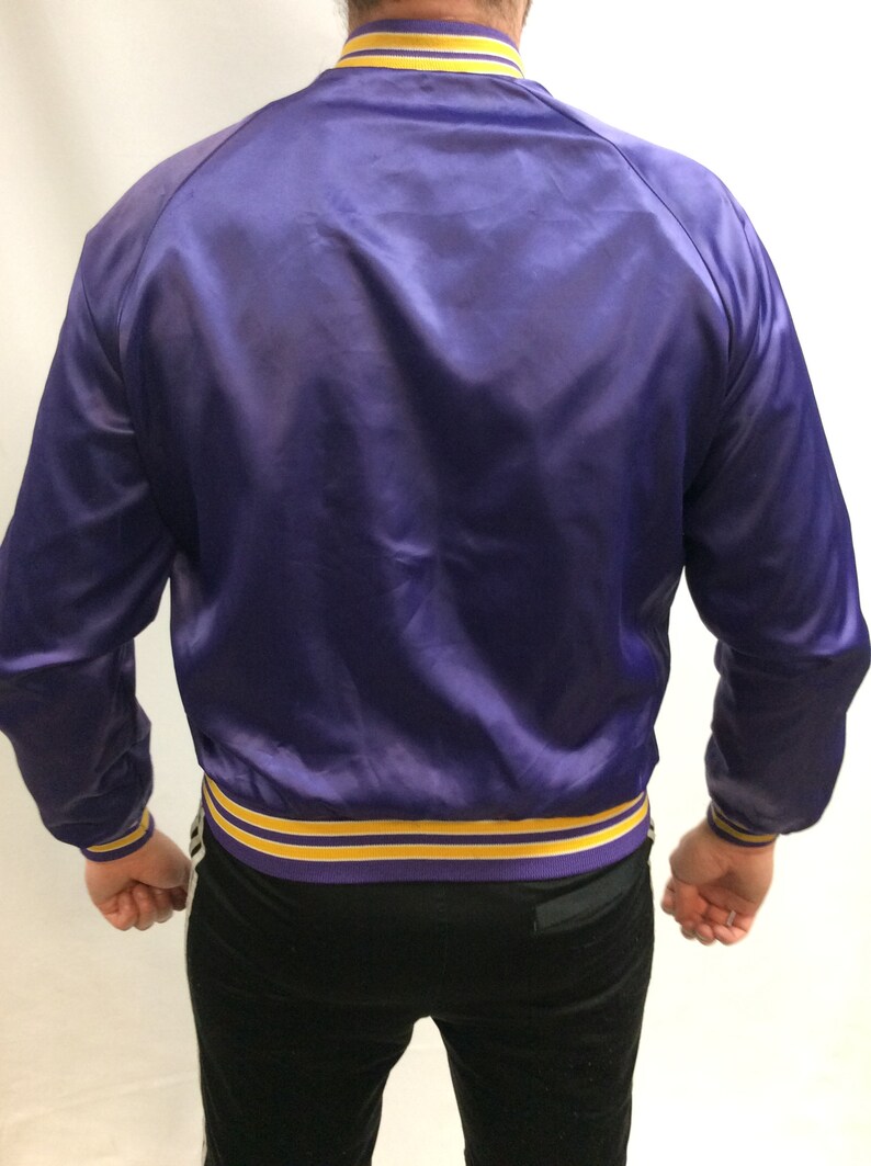 May include: A purple satin bomber jacket with yellow and purple striped trim around the collar, cuffs, and hem.