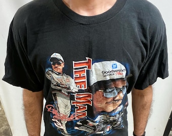 May include: Black t-shirt with a graphic of a man in a racing suit and a hat, with the words "THE MAN" in red. The shirt also features the words "Goodwrench Service Plus".