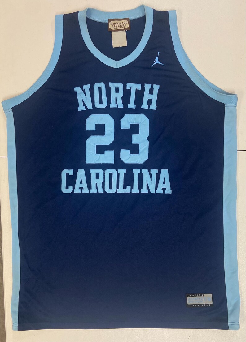 May include: Navy blue basketball jersey with light blue trim. The jersey features the words "NORTH CAROLINA" and the number "23" in light blue. A Jumpman logo is visible on the upper right chest.